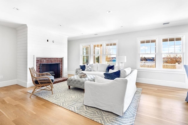 living area featuring a brick fireplace, baseboards, visible vents, and light wood finished floors