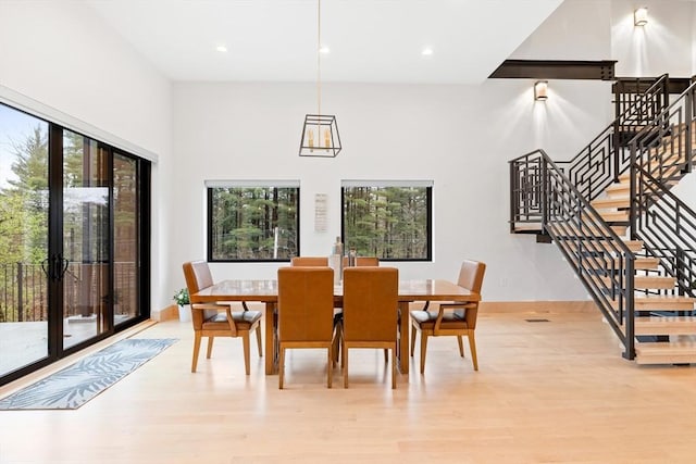 dining area featuring light wood-style flooring, recessed lighting, baseboards, stairs, and a towering ceiling