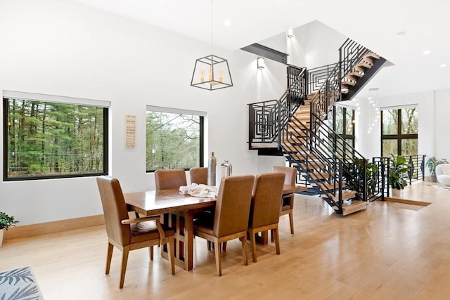 dining area featuring light wood-style floors, stairs, a chandelier, a towering ceiling, and baseboards