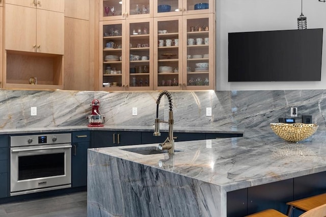 kitchen with stainless steel oven, a sink, light stone countertops, and decorative backsplash