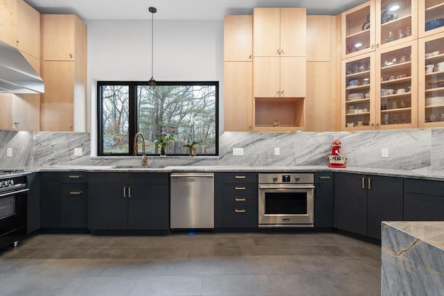 kitchen featuring appliances with stainless steel finishes, a sink, light brown cabinetry, light stone counters, and tasteful backsplash
