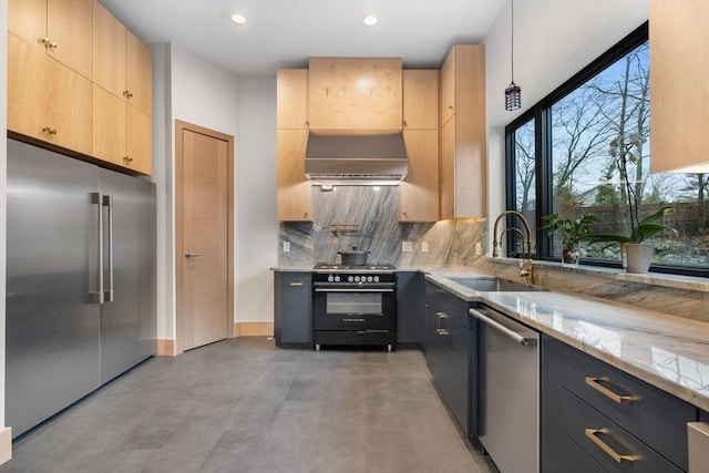 kitchen with premium appliances, a sink, exhaust hood, light stone counters, and light brown cabinetry