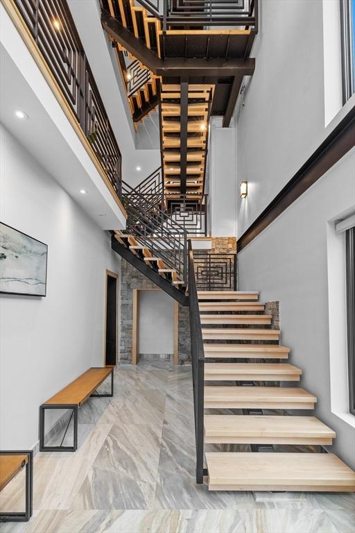 stairway with a towering ceiling, marble finish flooring, and recessed lighting