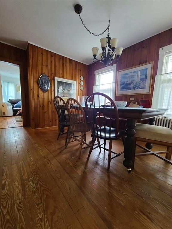 dining area featuring wood-type flooring, wooden walls, and a notable chandelier