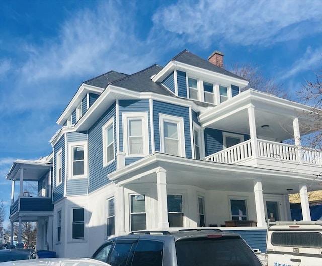 view of property exterior featuring a balcony, a chimney, and a porch