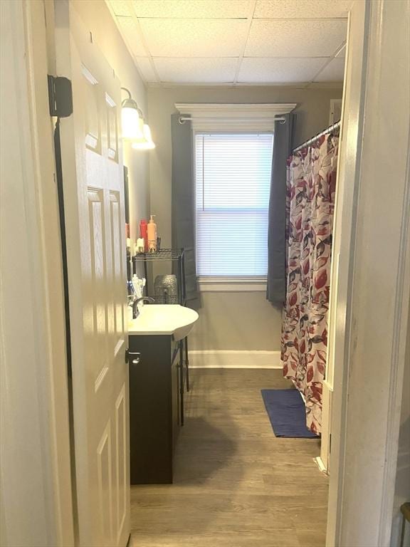 full bathroom featuring a shower with shower curtain, vanity, wood finished floors, a drop ceiling, and baseboards