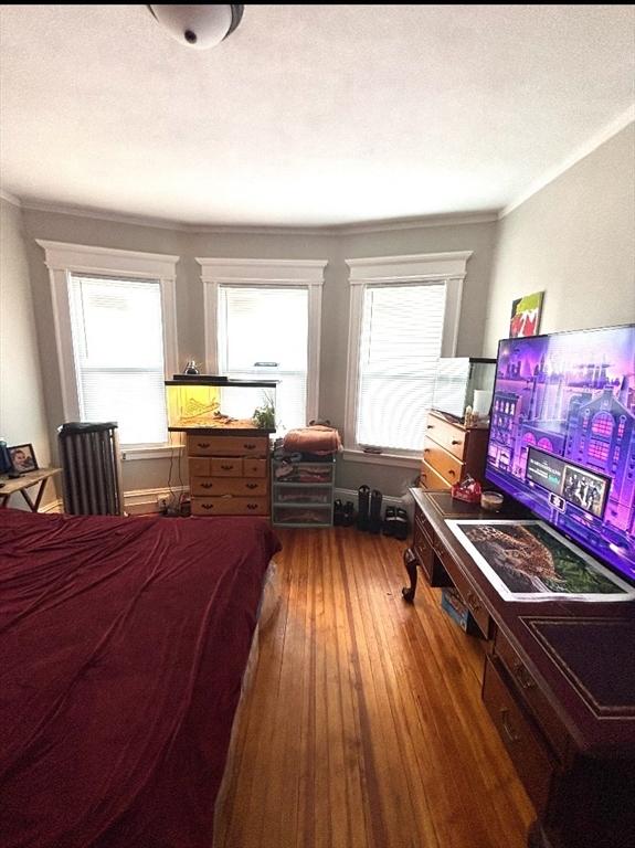 bedroom featuring a textured ceiling, crown molding, multiple windows, and wood finished floors