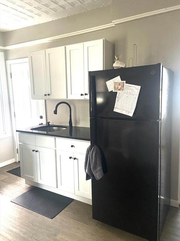 kitchen featuring dark wood finished floors, white cabinets, dark countertops, freestanding refrigerator, and a sink