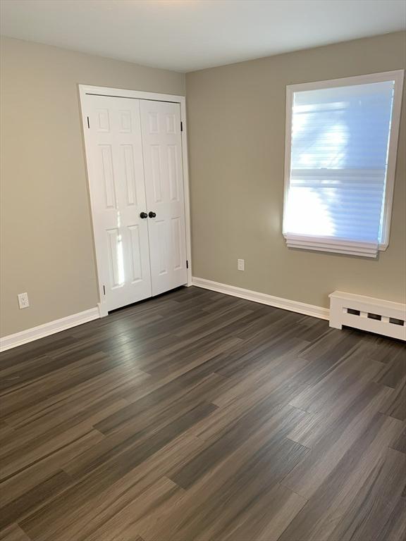 unfurnished bedroom featuring a baseboard heating unit, dark hardwood / wood-style flooring, and a closet