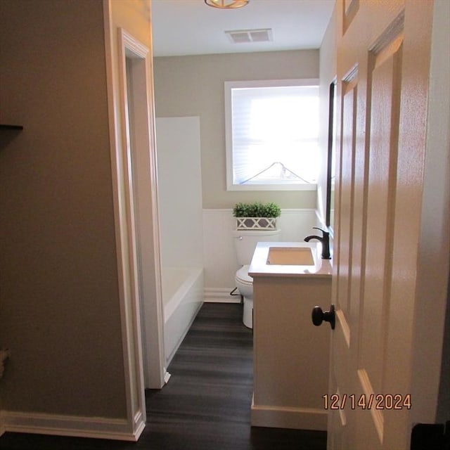 bathroom with toilet, vanity, a bath, and hardwood / wood-style flooring