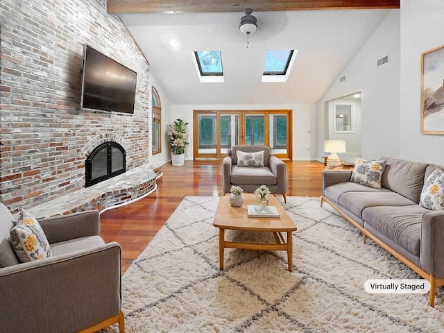 living room with ceiling fan, vaulted ceiling with skylight, a fireplace, and hardwood / wood-style floors