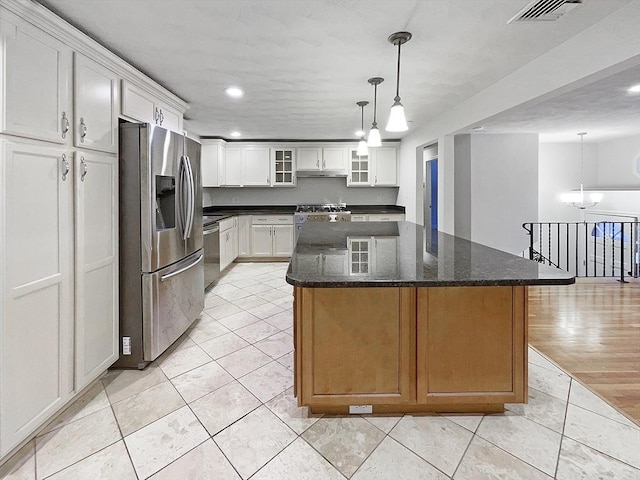 kitchen with pendant lighting, white cabinets, a kitchen island, stainless steel appliances, and dark stone counters