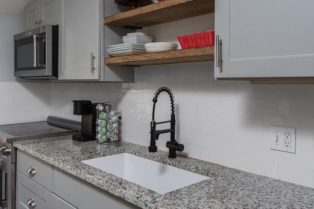 kitchen with appliances with stainless steel finishes, a sink, light stone counters, and open shelves