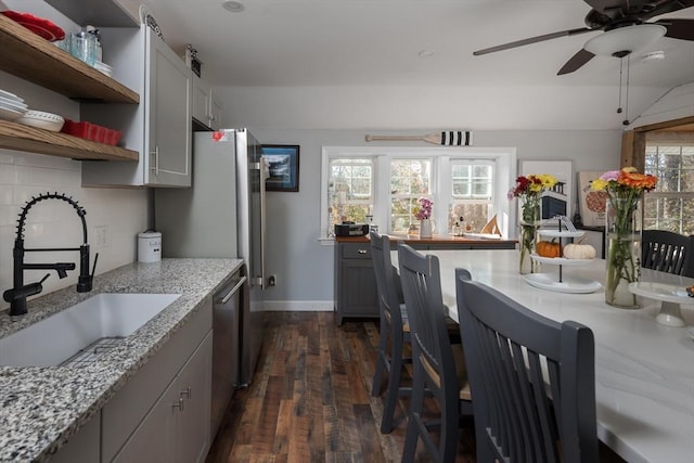 kitchen with light stone counters, gray cabinetry, a sink, dishwasher, and open shelves