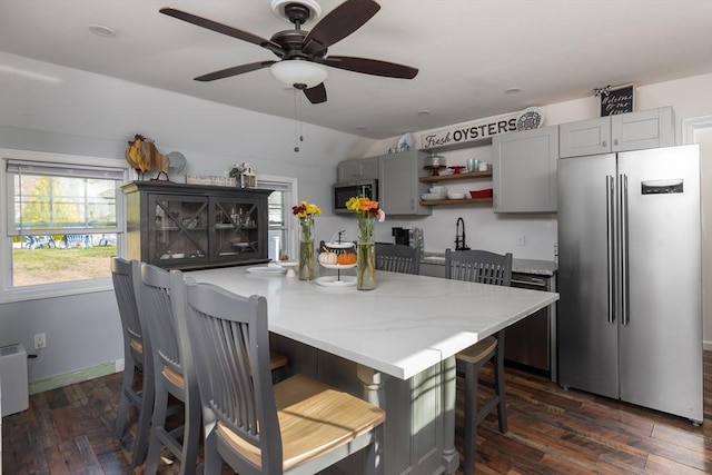 kitchen featuring appliances with stainless steel finishes, a breakfast bar, light countertops, gray cabinetry, and open shelves