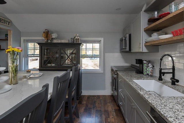 kitchen featuring dark wood finished floors, open shelves, stainless steel appliances, gray cabinetry, and a sink