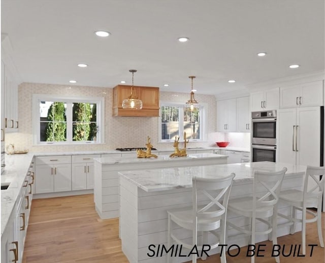 10 Webber Ave Unit 1A, Bedford, MA 01730 - kitchen featuring a center island, stainless steel double oven, white cabinets, tasteful backsplash, and light stone countertops