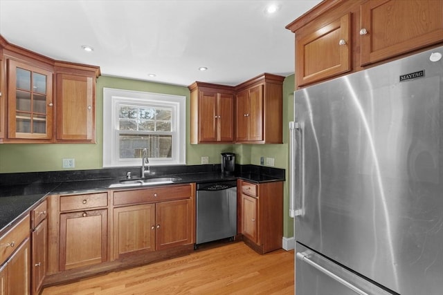 kitchen featuring sink, light hardwood / wood-style floors, dark stone counters, and appliances with stainless steel finishes