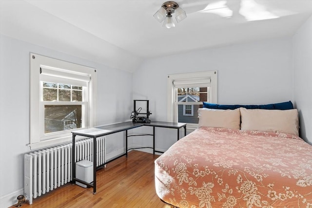 bedroom featuring radiator heating unit, light hardwood / wood-style flooring, and lofted ceiling