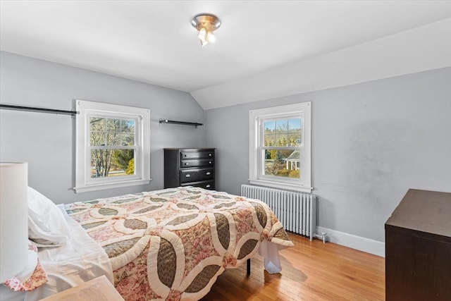 bedroom with radiator heating unit, light wood-type flooring, and lofted ceiling