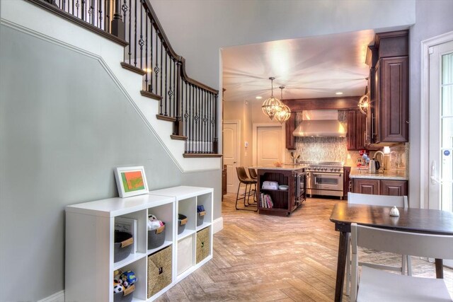 kitchen featuring light parquet floors, high end stainless steel range oven, tasteful backsplash, decorative light fixtures, and wall chimney exhaust hood