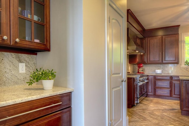 kitchen featuring high end stainless steel range, light stone counters, light parquet flooring, decorative backsplash, and wall chimney range hood