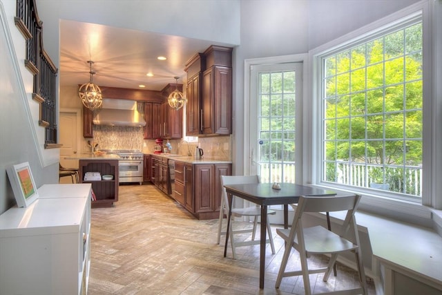 kitchen with stainless steel appliances, tasteful backsplash, decorative light fixtures, light parquet flooring, and wall chimney range hood