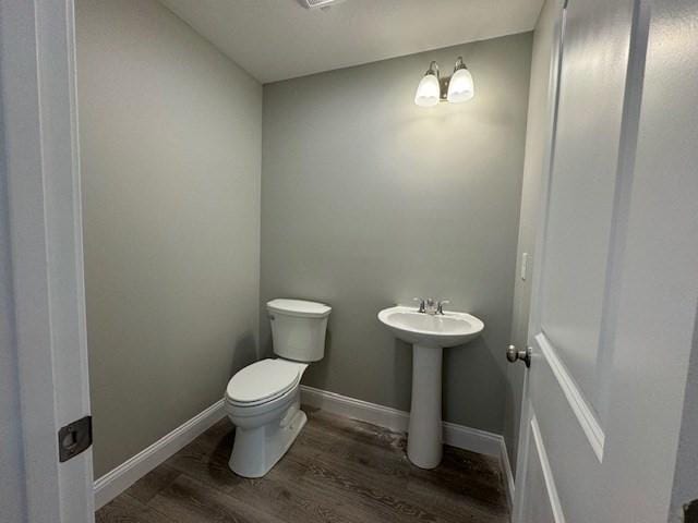 half bathroom with toilet, a sink, baseboards, and wood finished floors