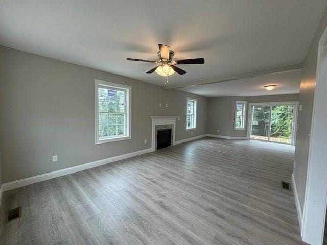 unfurnished living room with a wealth of natural light, a fireplace, visible vents, and wood finished floors