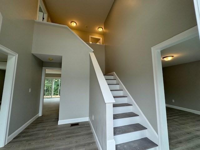 stairway featuring a towering ceiling, baseboards, and wood finished floors