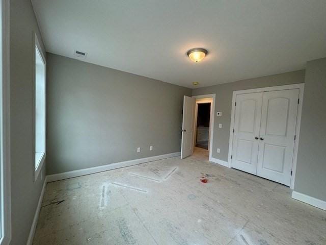 unfurnished bedroom featuring multiple windows, a closet, visible vents, and baseboards