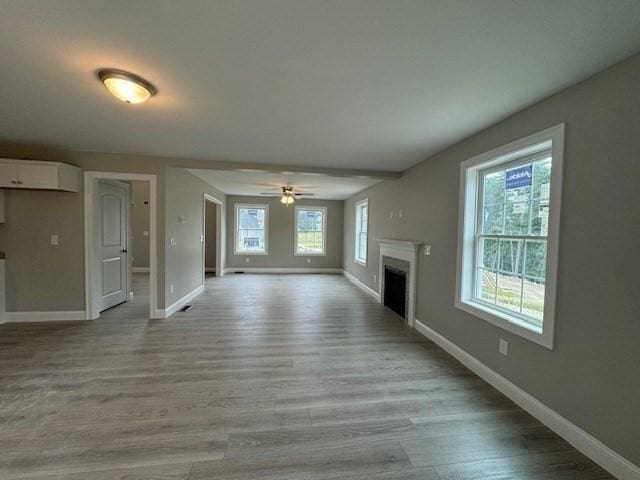 unfurnished living room with light wood-style floors, a wall mounted air conditioner, a fireplace, and baseboards