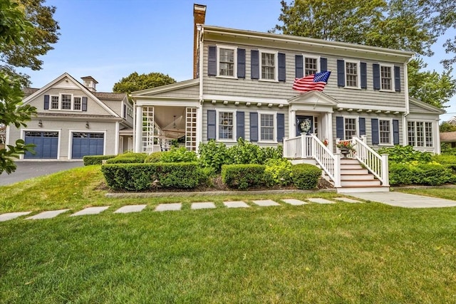 colonial house with a garage, a front lawn, a chimney, and aphalt driveway