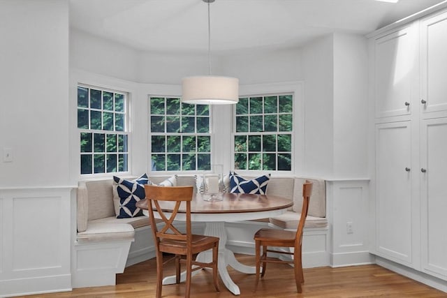 dining room featuring light wood-style floors, breakfast area, a decorative wall, and wainscoting