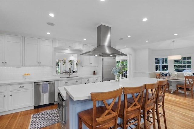 kitchen featuring island exhaust hood, stainless steel dishwasher, white cabinets, a sink, and a kitchen breakfast bar