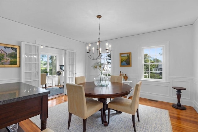 dining space with a decorative wall, a wainscoted wall, visible vents, light wood-style floors, and an inviting chandelier