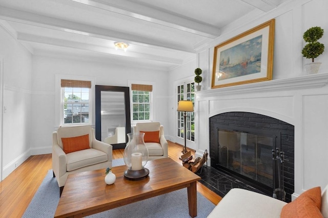 living area featuring baseboards, a glass covered fireplace, beam ceiling, and light wood-style floors