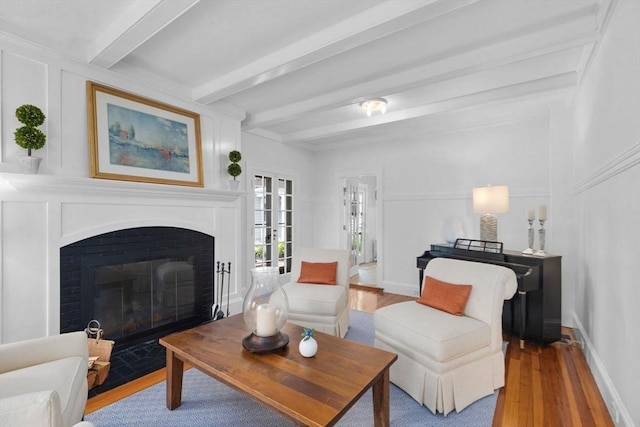 living room with a fireplace with flush hearth, a decorative wall, beam ceiling, and wood finished floors