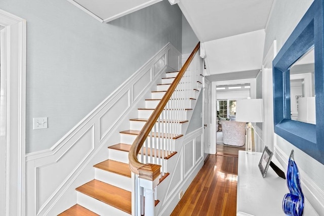 stairs featuring wood-type flooring, wainscoting, and a decorative wall