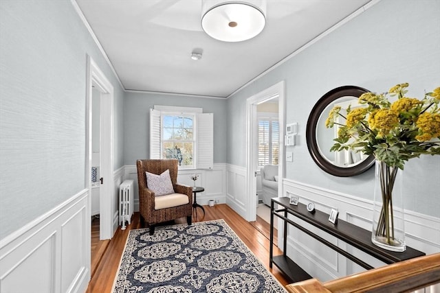 living area featuring ornamental molding, a wainscoted wall, radiator heating unit, and wood finished floors