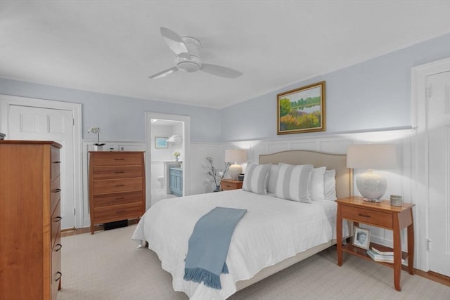 bedroom with wainscoting, ceiling fan, connected bathroom, and light colored carpet