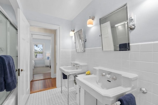 full bathroom featuring a shower with shower door, a wainscoted wall, a sink, tile walls, and tile patterned floors