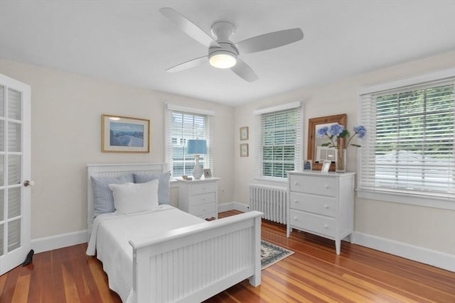 bedroom with radiator, multiple windows, baseboards, and wood finished floors