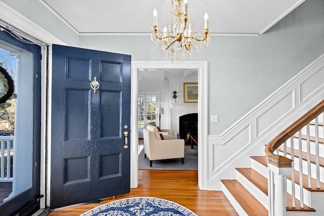 foyer with a decorative wall, a wainscoted wall, wood finished floors, stairs, and ornamental molding