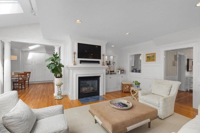 living room featuring ornamental molding, a fireplace with flush hearth, light wood-style flooring, and a decorative wall