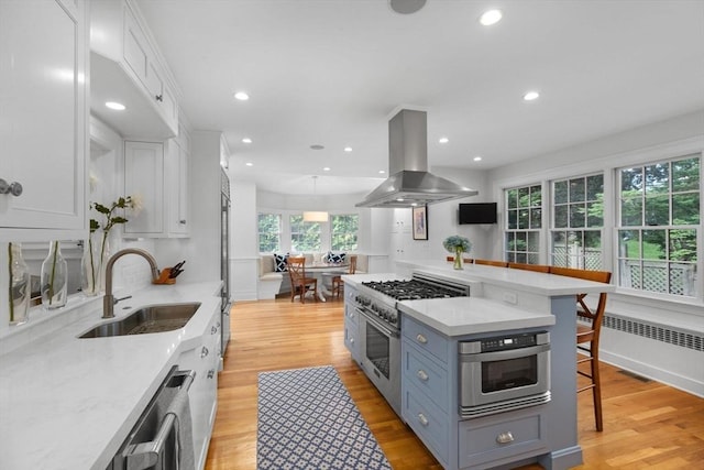 kitchen featuring island exhaust hood, stainless steel appliances, radiator, white cabinetry, and a sink