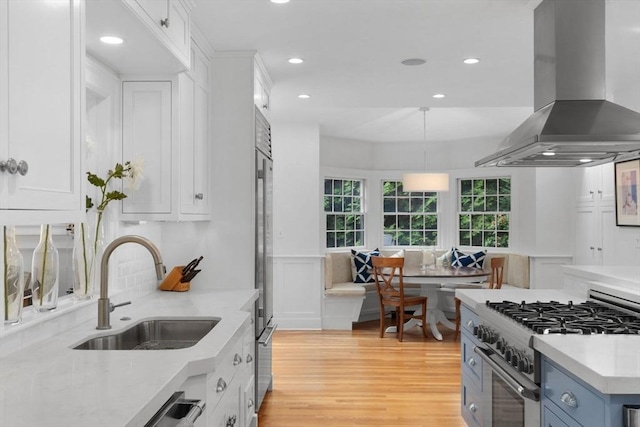 kitchen with a sink, exhaust hood, white cabinets, high end stainless steel range, and breakfast area