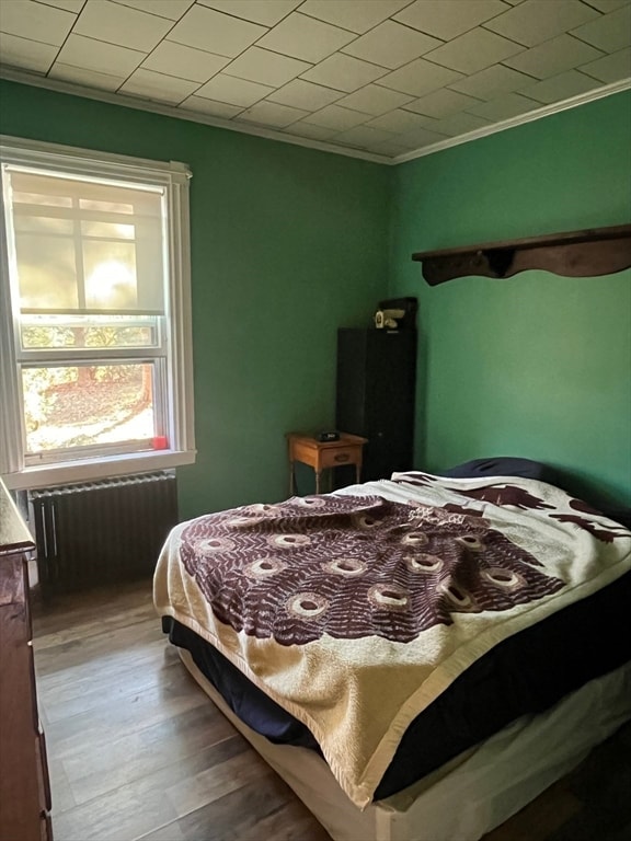 bedroom featuring radiator heating unit, hardwood / wood-style flooring, and ornamental molding