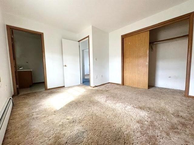 unfurnished bedroom featuring a closet, carpet flooring, ensuite bathroom, and a baseboard heating unit