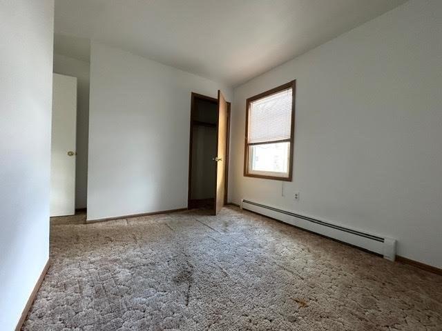 unfurnished bedroom featuring a baseboard heating unit and carpet